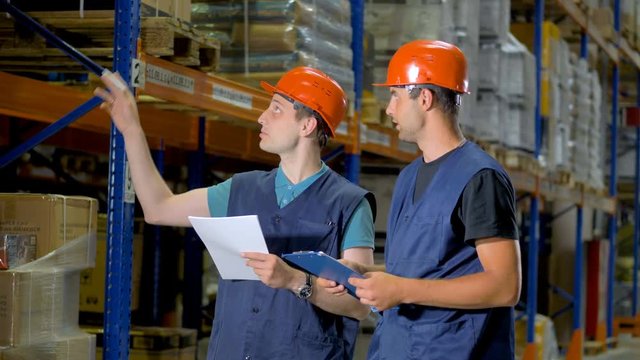 Two men discuss job matters inside a large warehouse. 