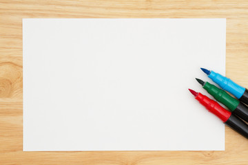 A red, green and blue watercolor brush marker with watercolor paper on wood desk