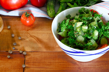 Tasty vegetable salad with cucumber, tomato and parsley on wooden kitchen table