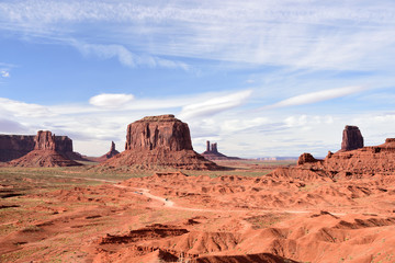 Monument Valley 's landmarks  of various feature against fluffy blue sky.