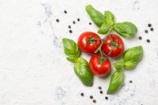 Fresh cherry tomatoes with basil leaves and black pepper on a stone table, top view with copy space