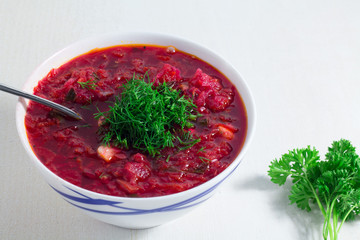 Red borscht soup in white bowl with parsley, top view, on white wooden background.