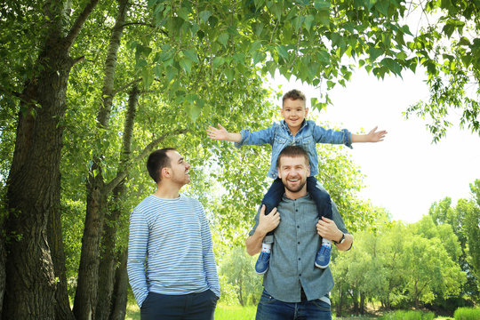 Smiling gay couple with son in park