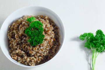 Vegan buckwheat porridge topped with fresh parsley in a bowl on a white table. Healthy breakfast