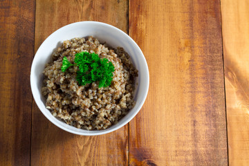 Buckwheat porridge in bowl with parsley on a wooden background closeup