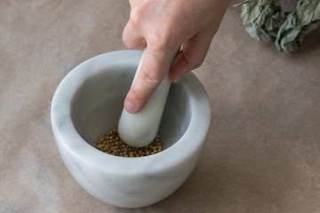 Mortar with coriander seeds and pestle in a woman's hand.