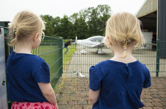 Two small identical twins girls are interested in watching the airplane