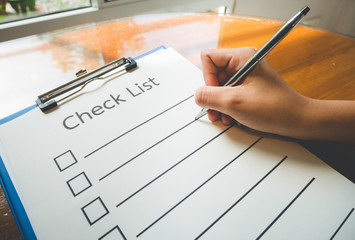 Close- up hand holding pen on check list paper and the format for filling in information in business concept,vintage style and softtone.