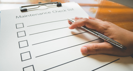 Close- up hand with pen on maintenance check paper and the format for filling in information in...