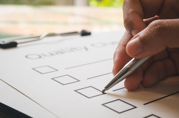 Close- up hand holding pen on quality check paper and the format for filling in information in...