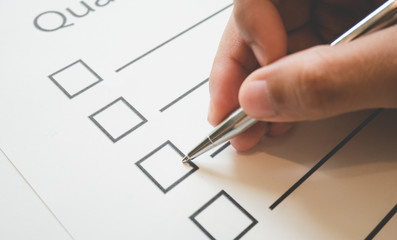 Close- up hand holding pen on quality check paper and the format for filling in information in business concept,vintage style and softtone.