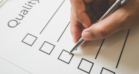 Close- up hand holding pen on quality check paper and the format for filling in information in business concept,vintage style and softtone.