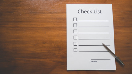 Flat lay and  Top view of Check list paper with pen on wooden table in business concept,vintage style.