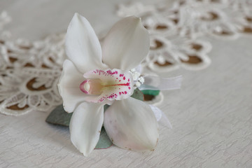Fototapeta na wymiar White orchid boutonniere small bouquet for buttonhole used for groom and wedding guests positioned on a white cloth, in natural light