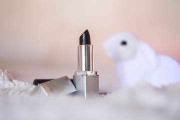 Black lipstick in silver tube and white bunny toy isolated on fluffy faux fur and soft pink background. Cruelty free concept. Blurred photography, high key, selective focus, perfect as background.