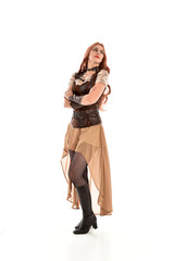 full length portrait of a red haired lady wearing steampunk inspired outfit, standing pose against a white background.