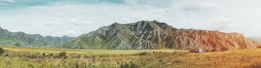 Stunning panoramic landscape of Altai mountains near river Katun and Kuyus district, Russia: native grasses meadows lit by sun, hills in distance, teal sky partly clouded