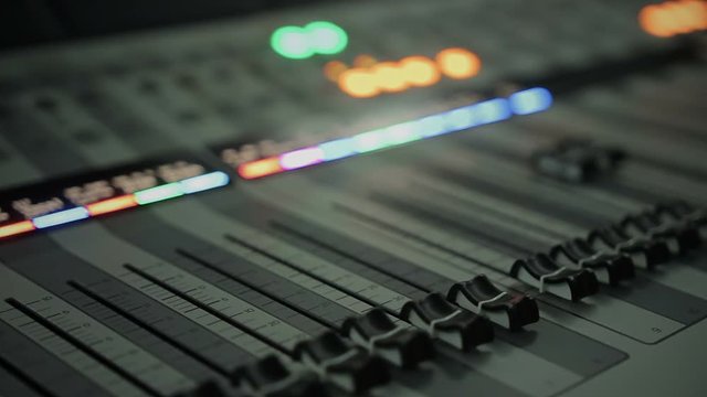 Close-up of audio mixing console with adjusting knobs and faders, mixer panel