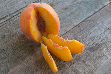 One ripe peache with slices and green leaf on the wooden background