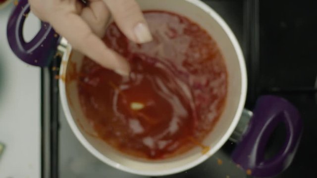 Hand dropping bouillon cube into pot of tomato soup, top view