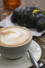 One white cup of cappuccino and black croissant on the talbe