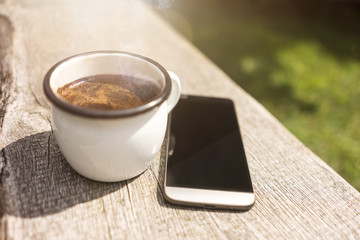 Coffee mug and mobile phone in the Sun