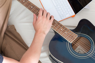 Junger Mann sitzend im Bett, Gitarre und Laptop