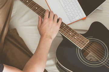 Junger Mann sitzend im Bett, Gitarre und Laptop