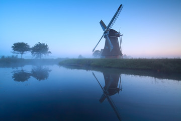 Dutch windmill by lake in dusk