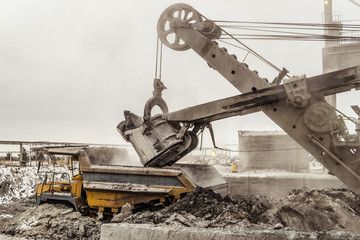 Bucket excavator loads into a large mining dump truck. Heavy industry.