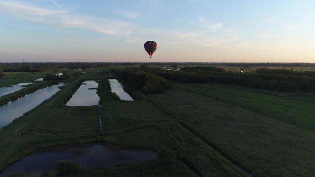 Aerial of hot air balloon bird view flying backwards from the sailing air balloon over nature reverse during sundown showing the bright late evening sun and the last light at horizon 4k resolution