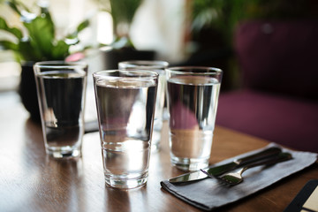 Close up photo of glasses with water on table in restaurant. Photo of four glasses with water and knife with fork on table in cafe