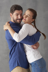Obraz premium Enjoy every moment together. Studio portrait of a loving young couple embracing each other while standing at grey wall with closed eyes. 
