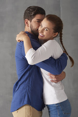 Enjoy every moment together. Studio portrait of a loving young couple embracing each other while standing at grey wall and looking at camera. 