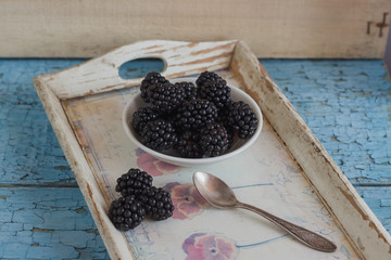 Fototapeta na wymiar Blackberry in the white bowl with a spoon on the wooden tray