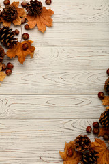 Flat lay frame of autumn leaves, cones and nuts on a wooden background.