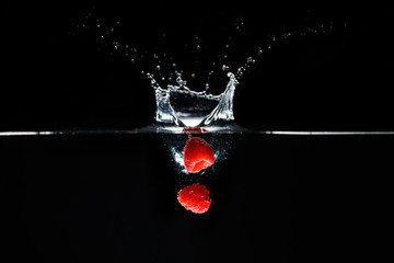 Two raspberrys falls deeply under water with a big splash.