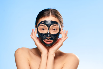 Fototapeta premium Beautiful young woman on a blue background in a black coal cosmetic face mask