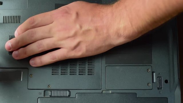 Laptop repair. The man opens the back cover of the laptop with a screwdriver. Hands close up