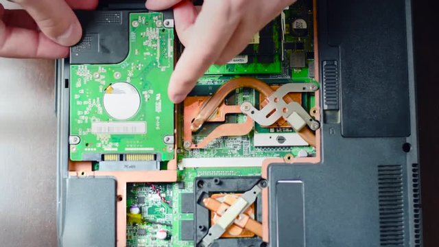 Replacing the hard drive in the laptop. A man with a screwdriver twists and pulls the hard drive.