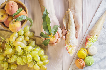 Hands of a young woman holding a cake and peach, making a choice between them. Woman making a...