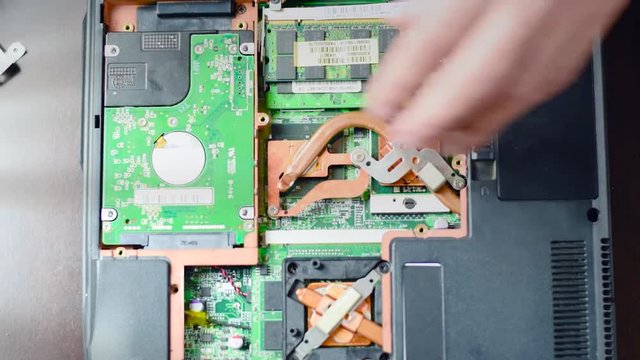 Replacing the hard drive in the laptop. A man with a screwdriver twists and pulls the hard drive.