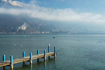 Jetty on the French Annecy lake, surrounded by the mountains under the clouds.