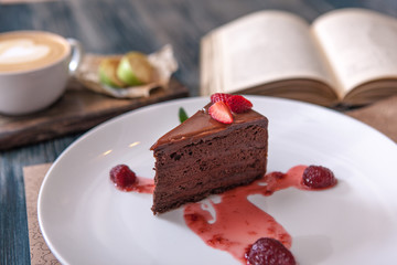 piece of cake with strawberries on a plate with a Cup of coffee on wooden table near old books
