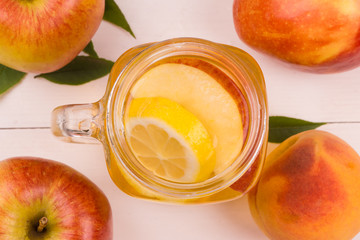Sparkling White Peach Sangria apples, oranges and lemons on a white rustic wooden background. Jug...