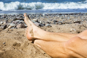 closeup of mans feet lying on the beach