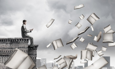 Man using smartphone and many books flying in air