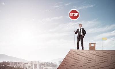 Caucasian businessman on brick house roof showing stop road sign