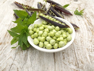 Peeled young green peas in a bowl and a bunch of mint