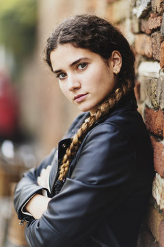 Portrait of teenage girl in leather jacket leaning against brick wall